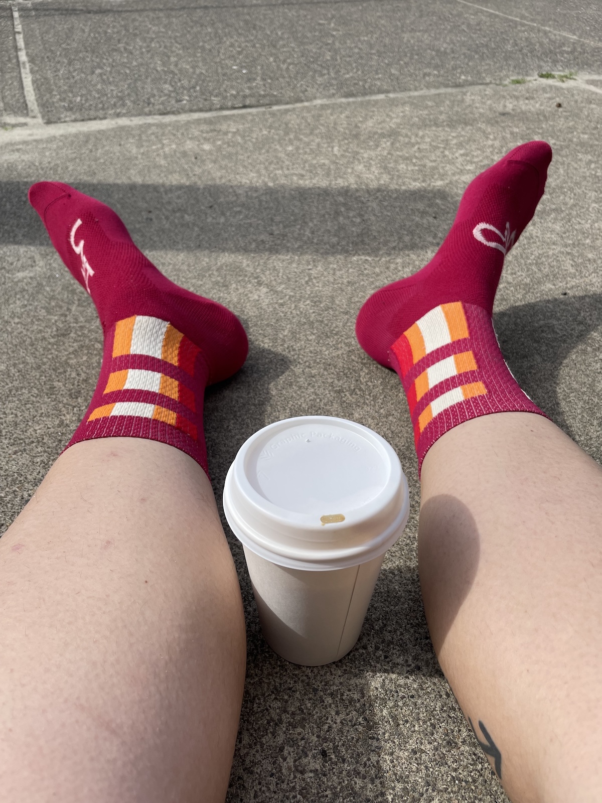 The author sits on the ground stretching her legs with a cup of coffee between them.