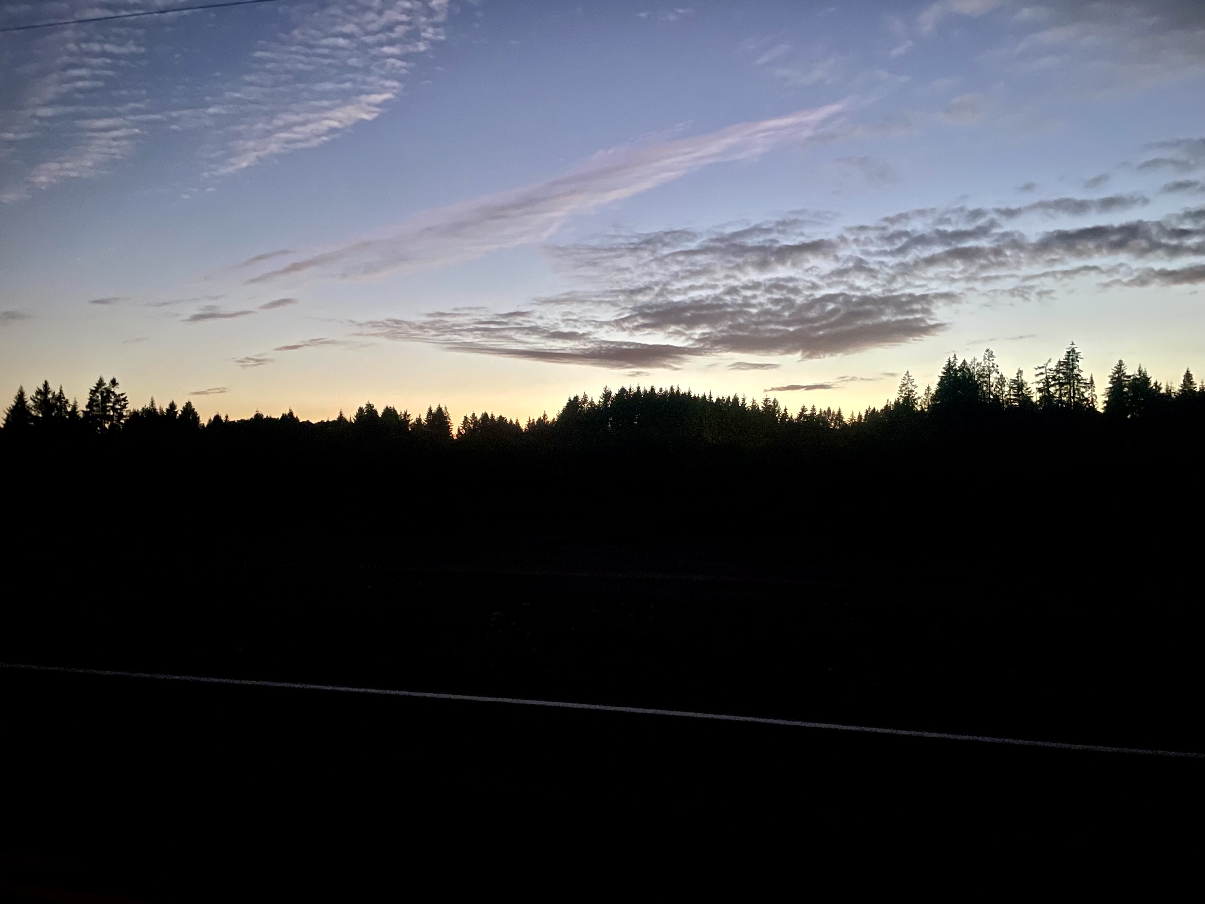 Farmland and trees are shadowed by the recently set sun while the sky remains some fading color.